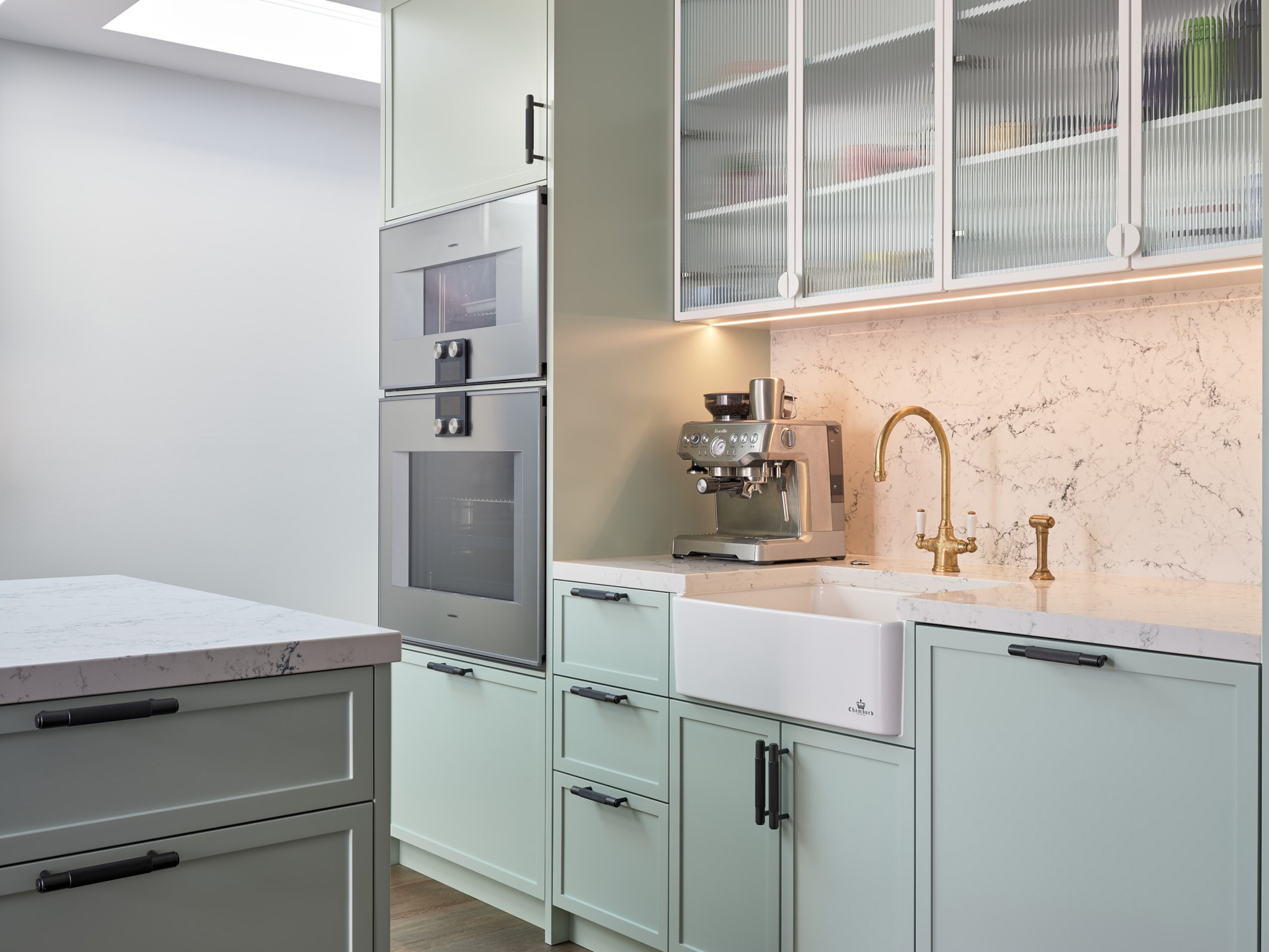A custom Elite Joinery kitchen — soft-green cabinetry, a marble splashback and brushed-brass tapware in a Sydney home.