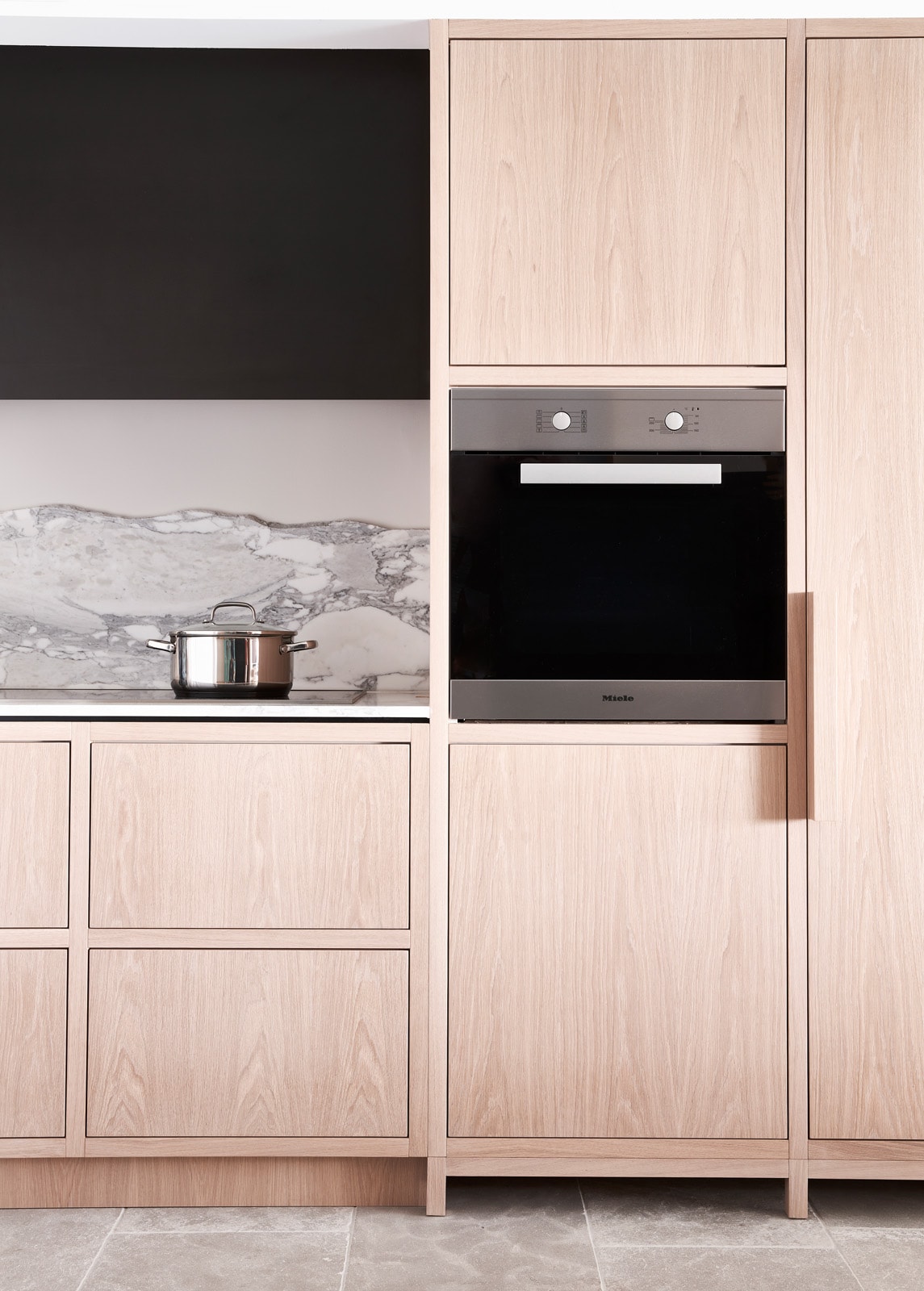 Custom kitchen in pale oak with a marble splashback and integrated appliances.