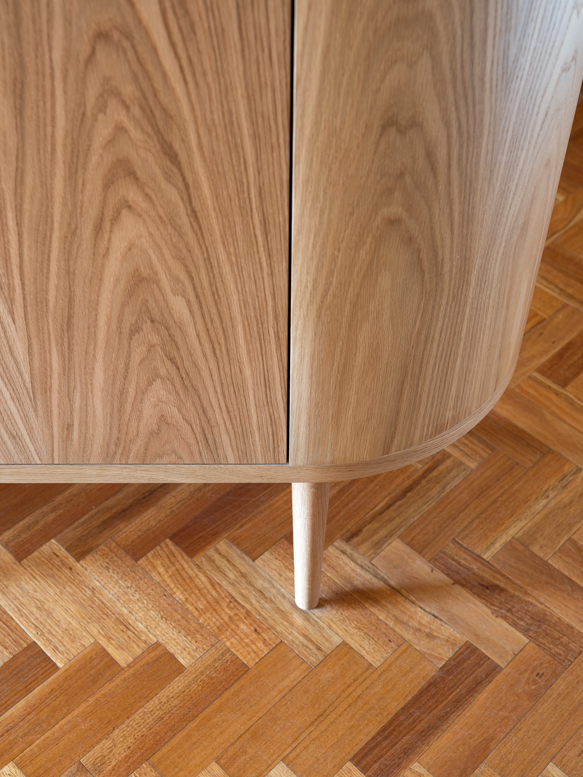 Detail of a curved, hand-finished oak cabinet by Elite Joinery, standing on a parquet floor.