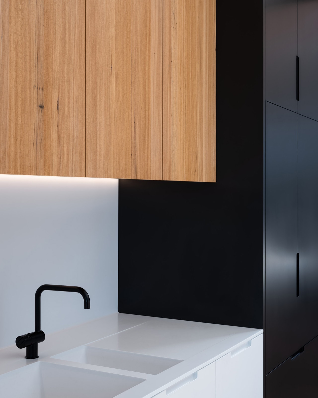 Custom terrace-house kitchen with timber cabinetry, white stone benchtop and a black tapware detail.