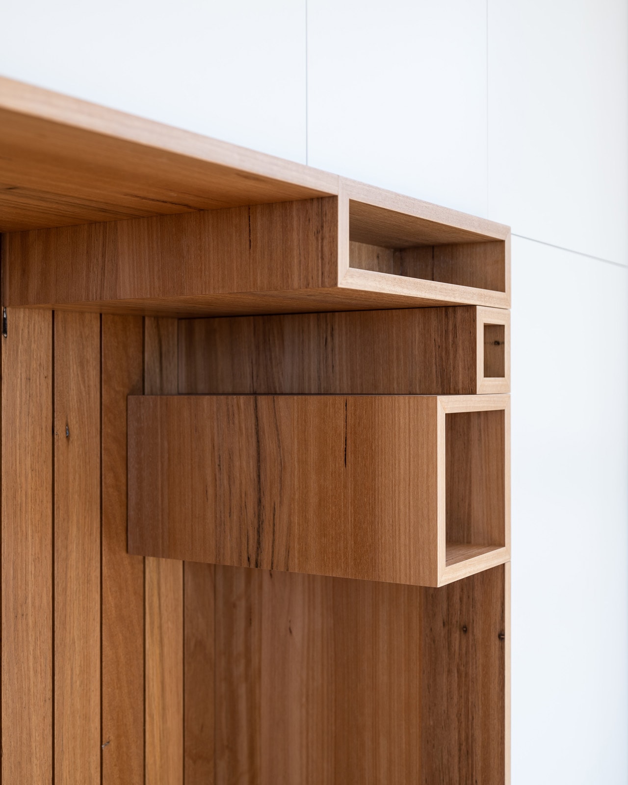 Solid-timber library shelving boxes set into a full-height white cabinetry wall.