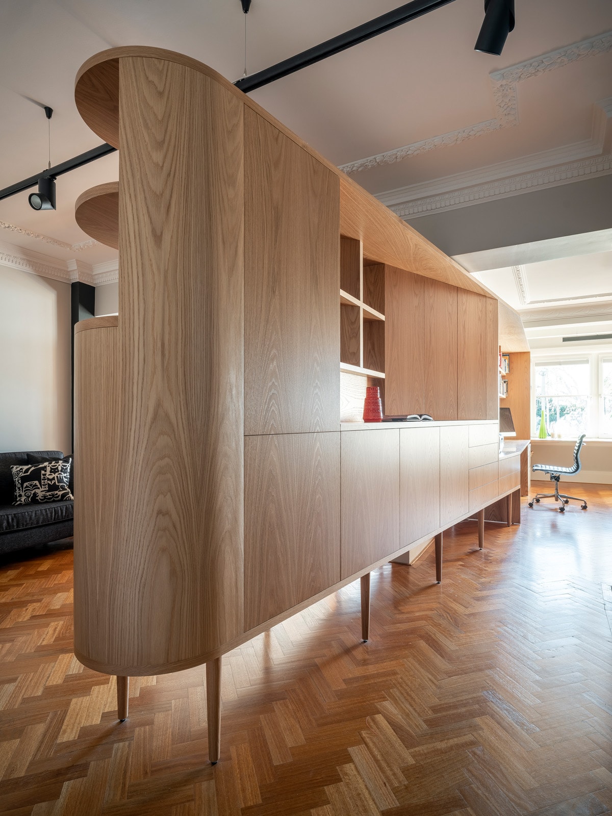 Curved oak storage cabinetry standing on a herringbone parquet floor.